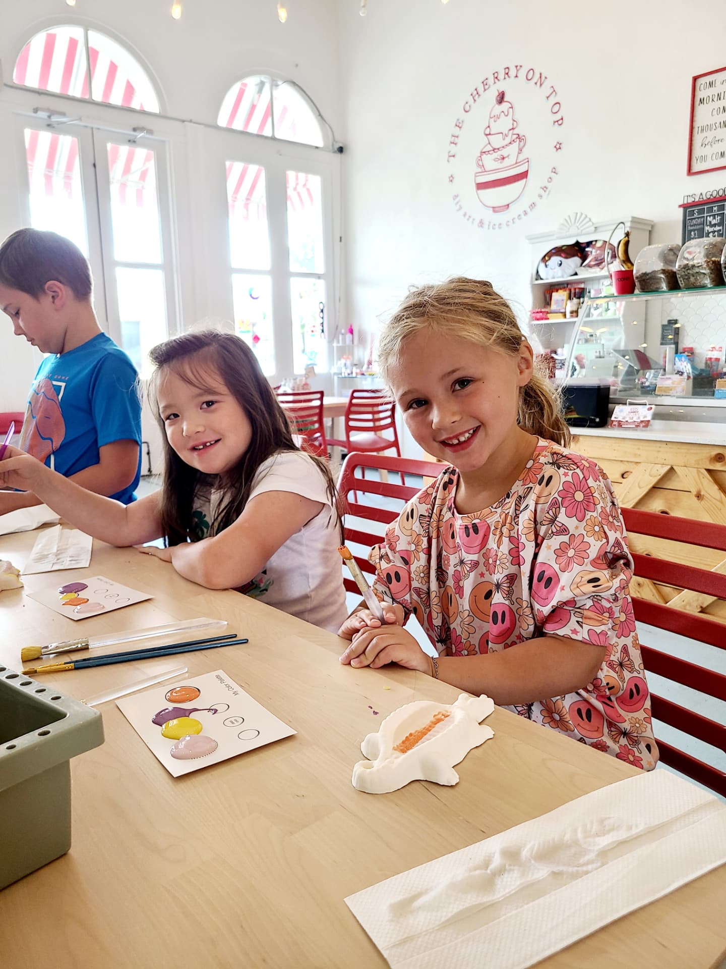 Children painting pottery together during a creative class at The Cherry on Top