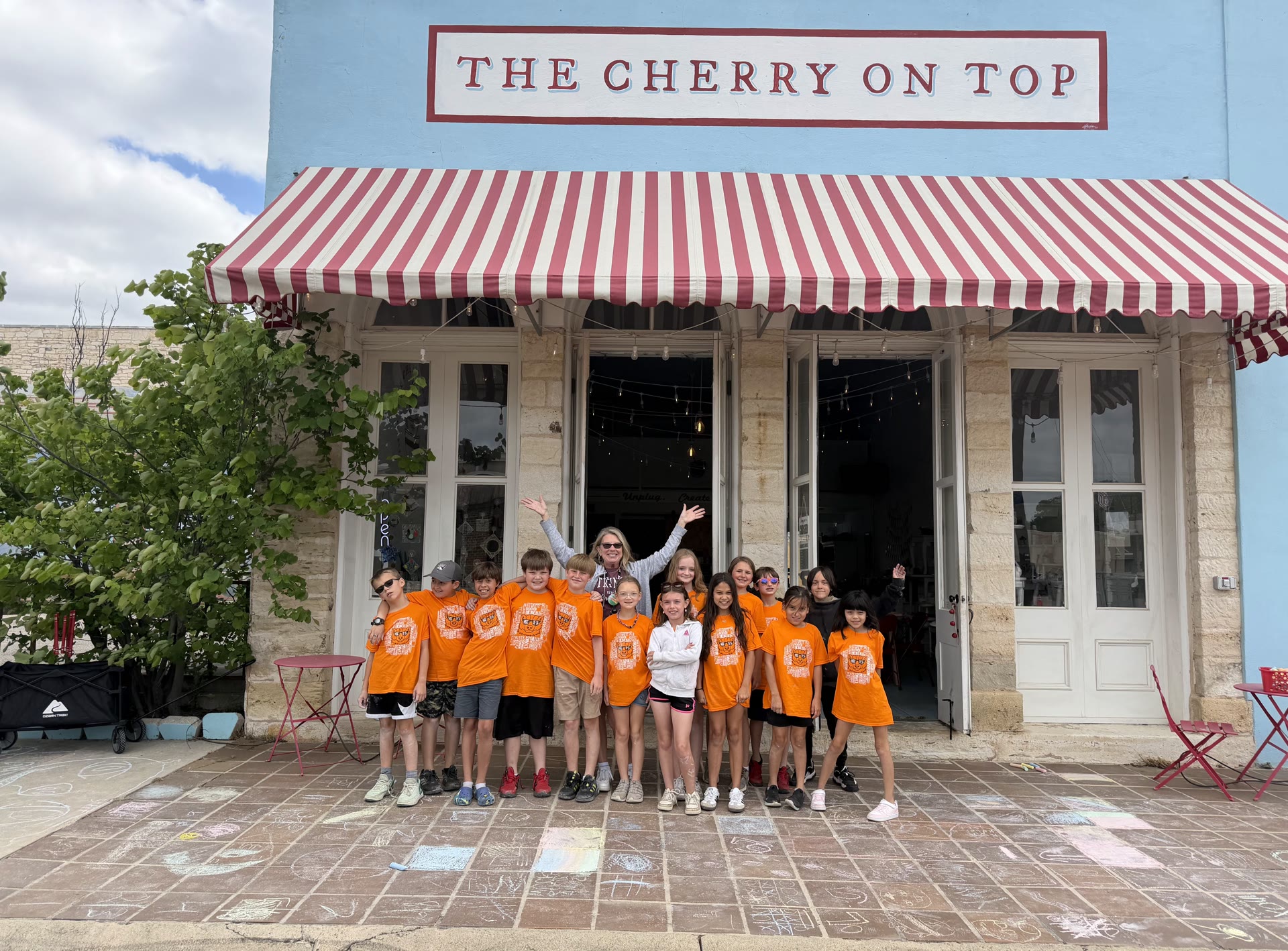 A school field trip group posing in front of The Cherry on Top's blue storefront and striped awning in Lampasas, Texas