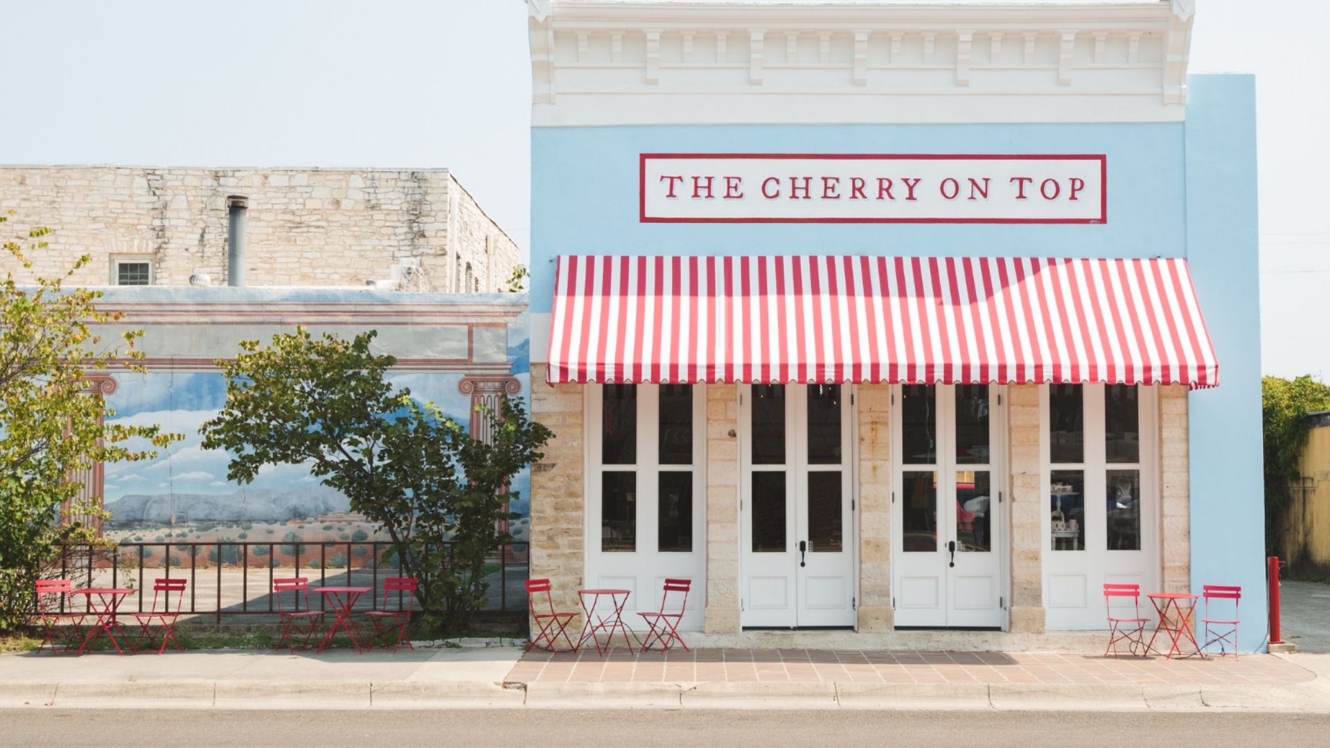 The blue historic storefront of The Cherry on Top with its red and white striped awning in downtown Lampasas, Texas