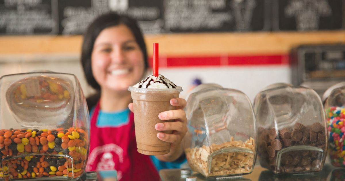 A chocolate milkshake topped with whipped cream and chocolate syrup, held out over the ice cream counter